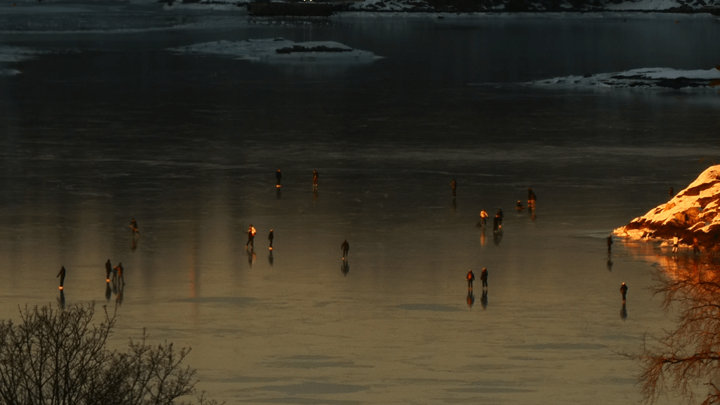 Folkemengde på isen i det varme lyset fra en solnedgang. Noen holmer og skjær synes i bildet.