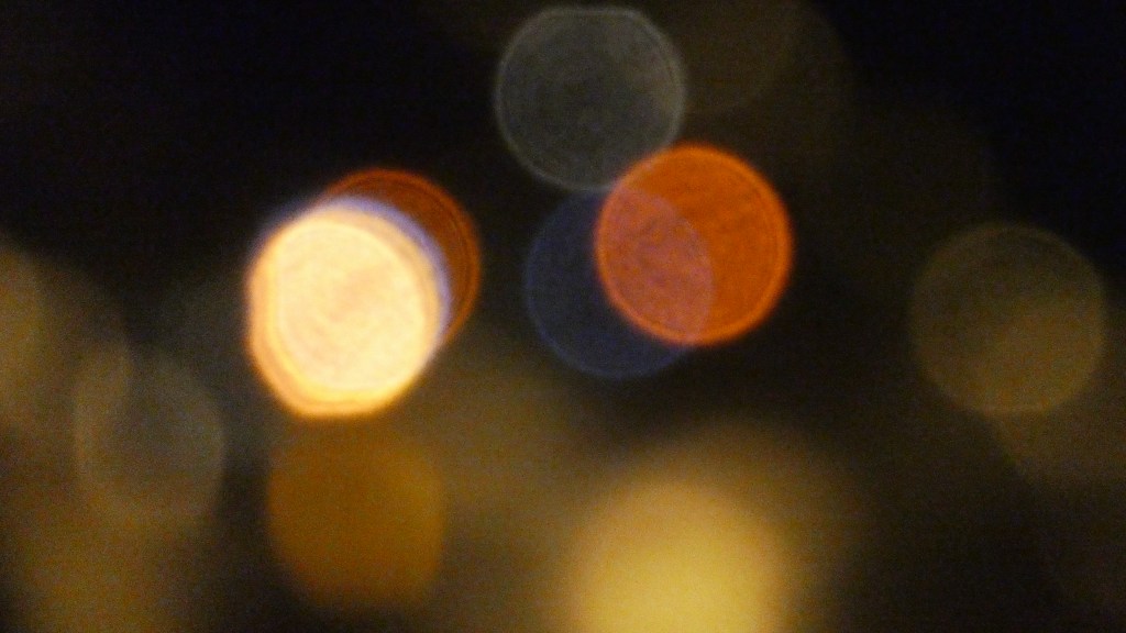 Uskarpt, stemningsfullt bilde av fargerike lys gjennom en vindusrute i mørket.