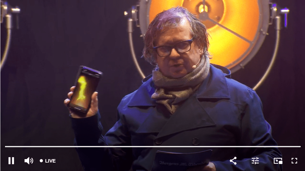 Skjermbilde fra lysfesten. En av de som presenterer holder opp en mobil med en video av en fakkelflamme.